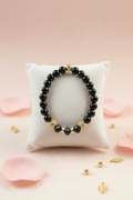 Black onyx and gold beaded bracelet on a white velvet jewelry pillow surrounded by pink rose petals
