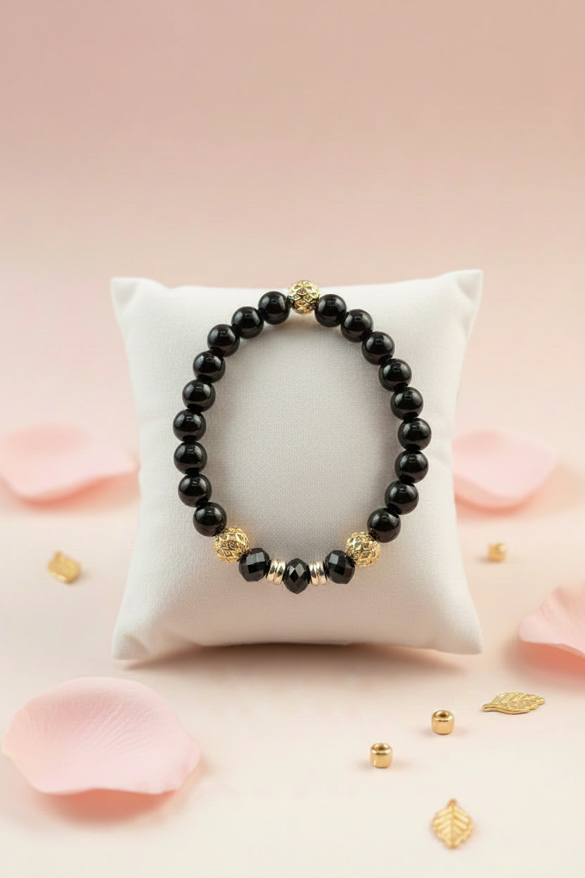Black onyx and gold beaded bracelet on a white velvet jewelry pillow surrounded by pink rose petals