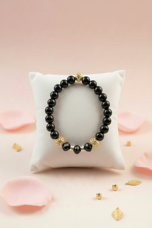 Black onyx and gold beaded bracelet on a white velvet jewelry pillow surrounded by pink rose petals
